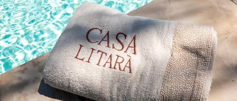Une serviette ornée d’une broderie « CASA LITARA », posée sur une surface en béton près d’une piscine.