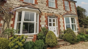A two-story stone house with a bay window, a front door, and a small porch area. - Millmead House (Weymouth)