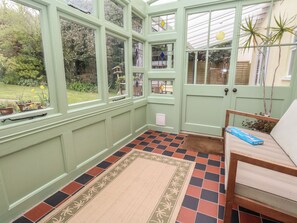 A conservatory with large windows, a patterned rug, and a chair. - Millmead House (Weymouth)
