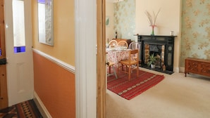 A dining area with a table, chairs, a chandelier, a fireplace, and a patterned wall. - Millmead House (Weymouth)