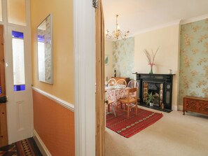 A dining area with a table, chairs, a chandelier, a fireplace, and a patterned wall. - Millmead House (Weymouth)
