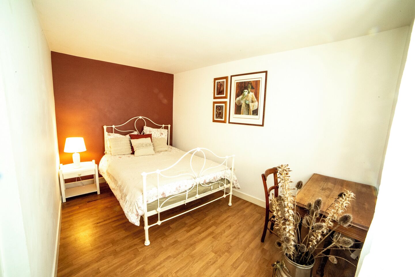 Une chambre à coucher avec un lit, une table de chevet, une lampe et une petite table décorée de fleurs séchées.