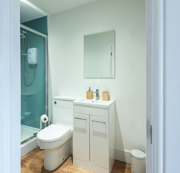 A bathroom with a toilet, a sink, a mirror, and a shower.