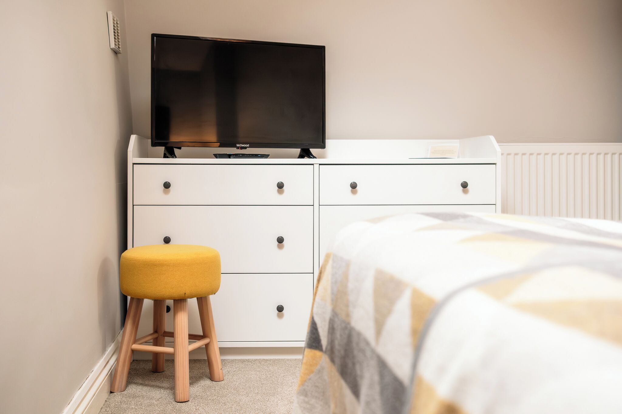 A bedroom with a bed, a TV on a dresser, and a stool.