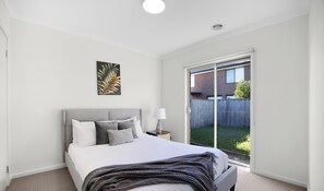 A bedroom with a bed, a nightstand, a lamp, a window, and a door. - Contemporary 4BR2BA house in Point Cook with Study (Point cook)