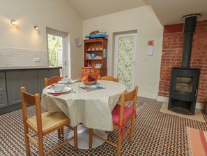 A dining area with a round table, chairs, a bookshelf, a clock, and a fireplace. - Millmead House Annex (Weymouth)