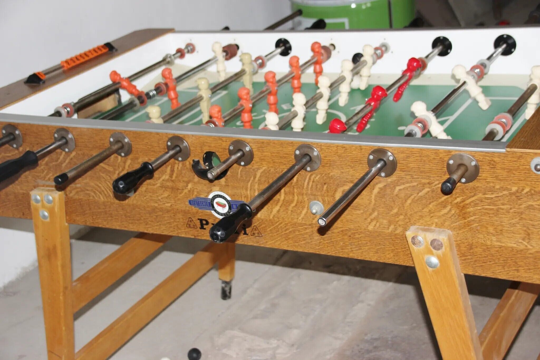 A wooden foosball table with multiple rods and figures, a visible logo, and a green playing surface.