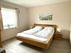 Een slaapkamer met een houten bed, twee nachtkastjes, een raam met gordijnen en een schilderij aan de muur.