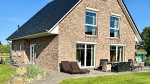 Una casa de dos pisos con fachada de ladrillo, ventanas grandes y un patio con mobiliario exterior.