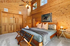 Ein Schlafzimmer in einer Holzhütte mit einem Bett, einem Deckenventilator, einem Gemälde und einem kleinen Tisch mit einer Lampe.
