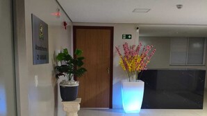 Un pasillo con mostrador de recepción, una puerta de madera, un letrero que indica la zona de recepción y una planta con flores.