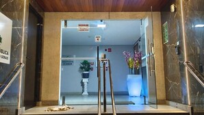 Entrada de un hotel con techo de madera, paredes de mármol, un cartel que indica el segundo piso y una escalera con barandilla.