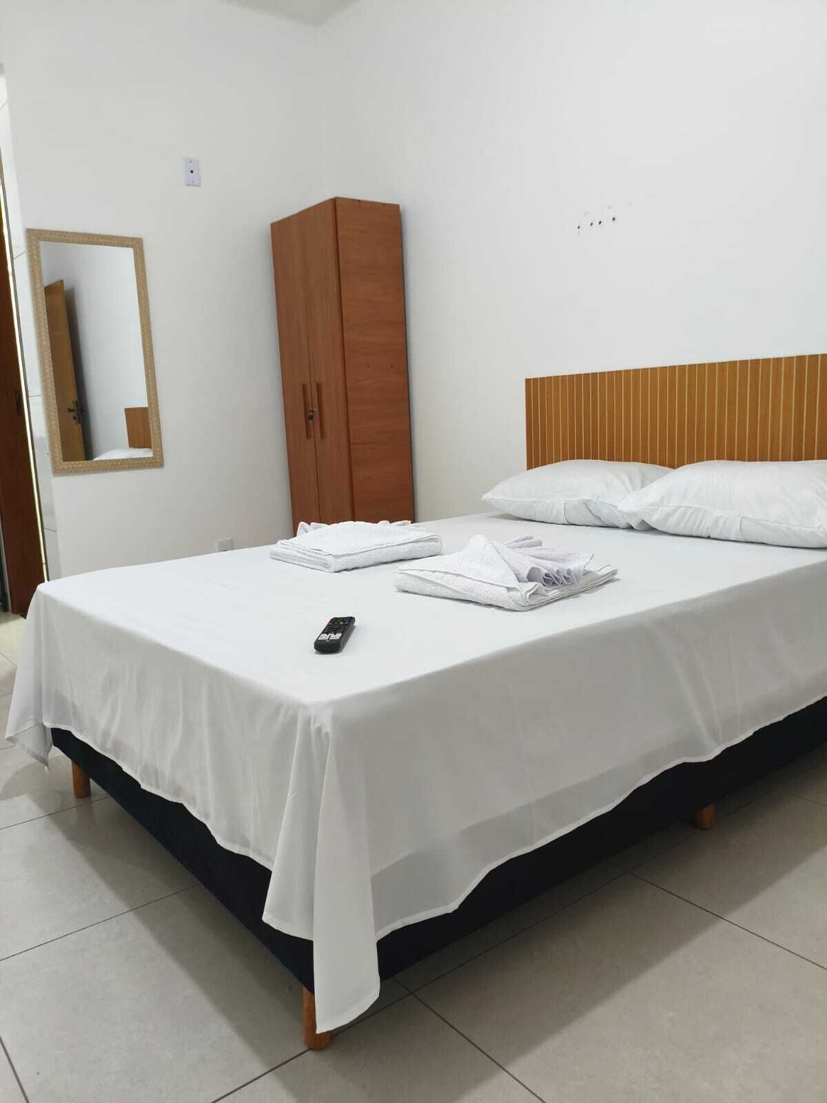 Uma cama bem arrumada com lençóis brancos, cabeceira de madeira e guarda-roupa de madeira.