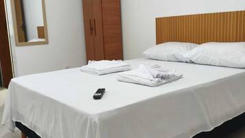 Uma cama bem arrumada com lençóis brancos, cabeceira de madeira e guarda-roupa de madeira.