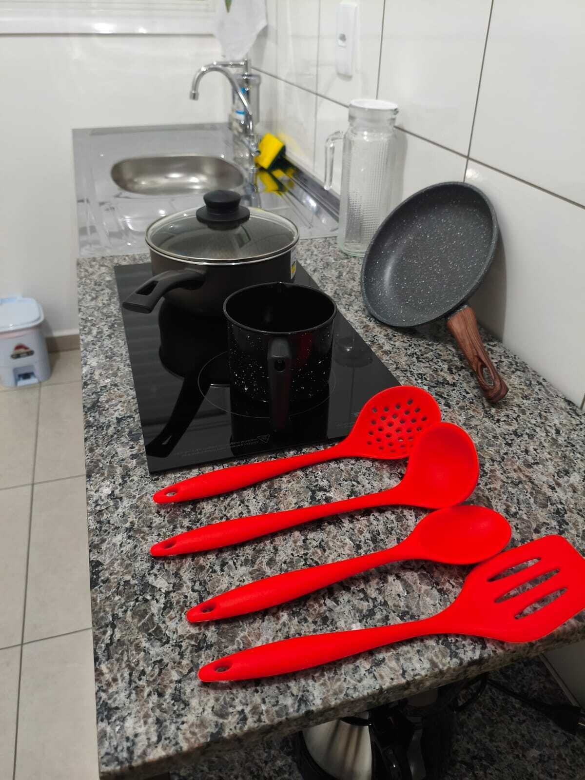 En köksbänk med en kastrull, en stekpanna, en mugg och röda stekspadar.