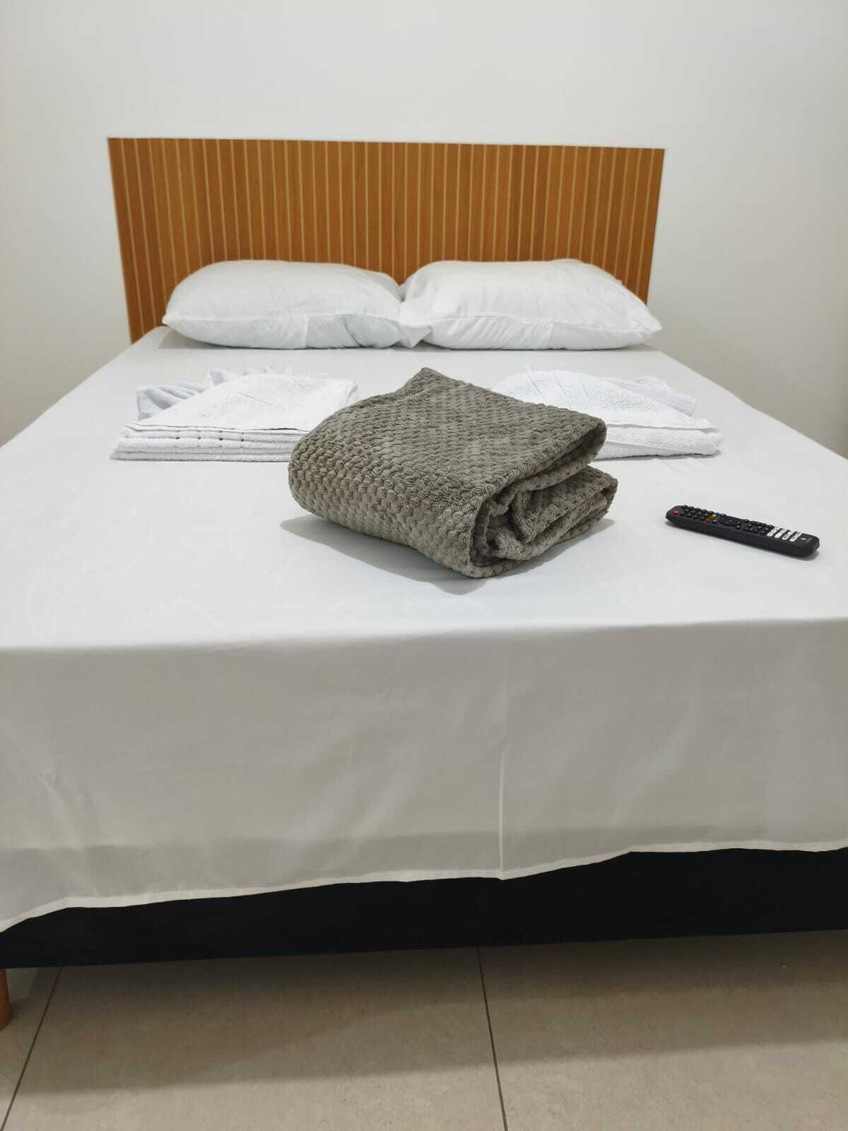 A neatly made bed with a folded blanket, pillows, and a remote control on the bed.