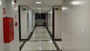 Un pasillo con suelo de baldosas, señales de salida de emergencia y un extintor rojo a la izquierda.