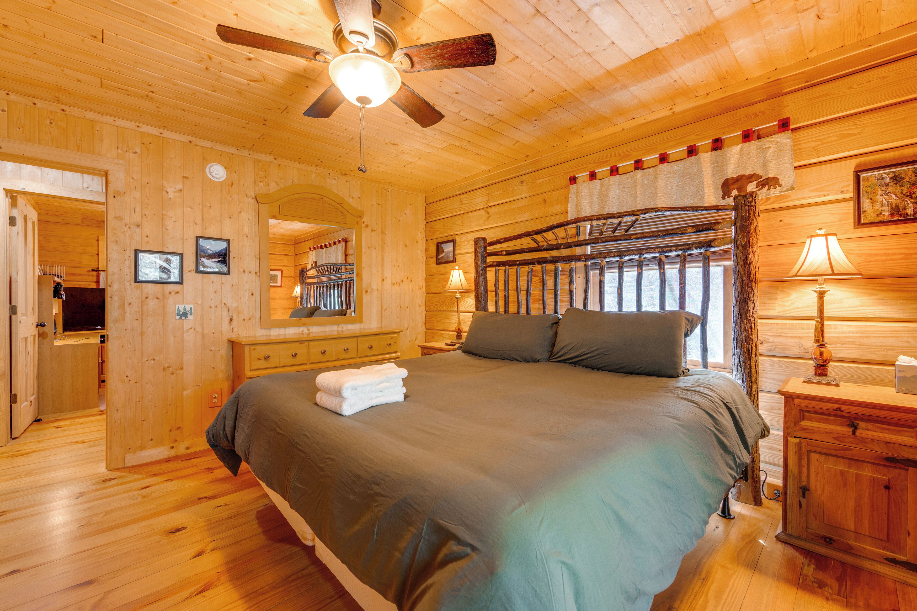 A wooden cabin-style bedroom with a bed, a ceiling fan, a nightstand with a lamp, and a wooden wardrobe.