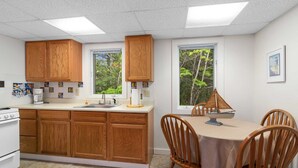 Une cuisine avec des meubles de rangement en bois, une table à manger avec des chaises et une fenêtre donnant sur des arbres.