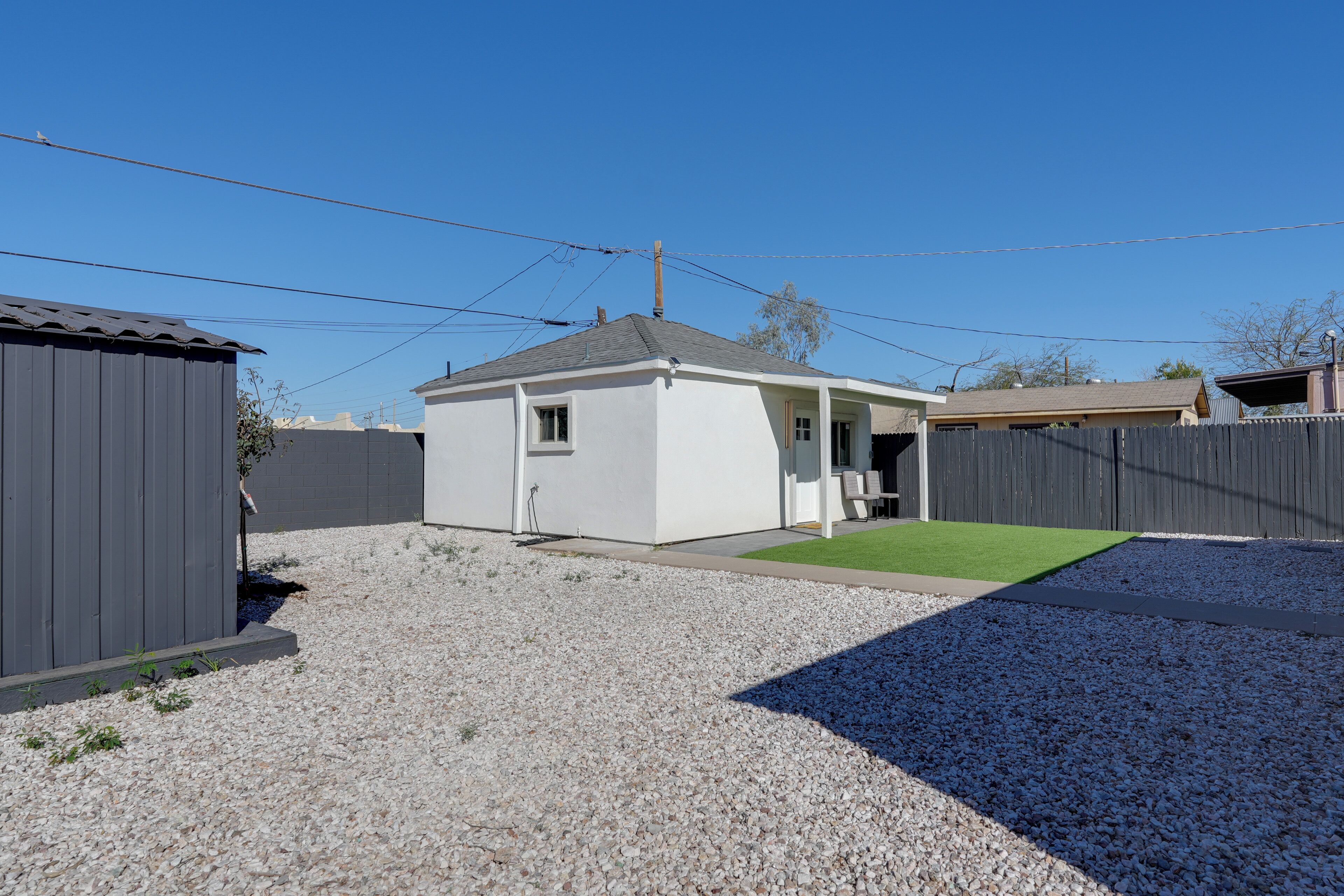 A residential backyard with a white shed, a small house, and a wooden fence.