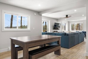 A modern living room with a wooden dining table, blue sofa, and large windows.