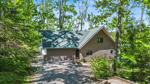 A two-story cabin with a green roof, surrounded by dense forest.