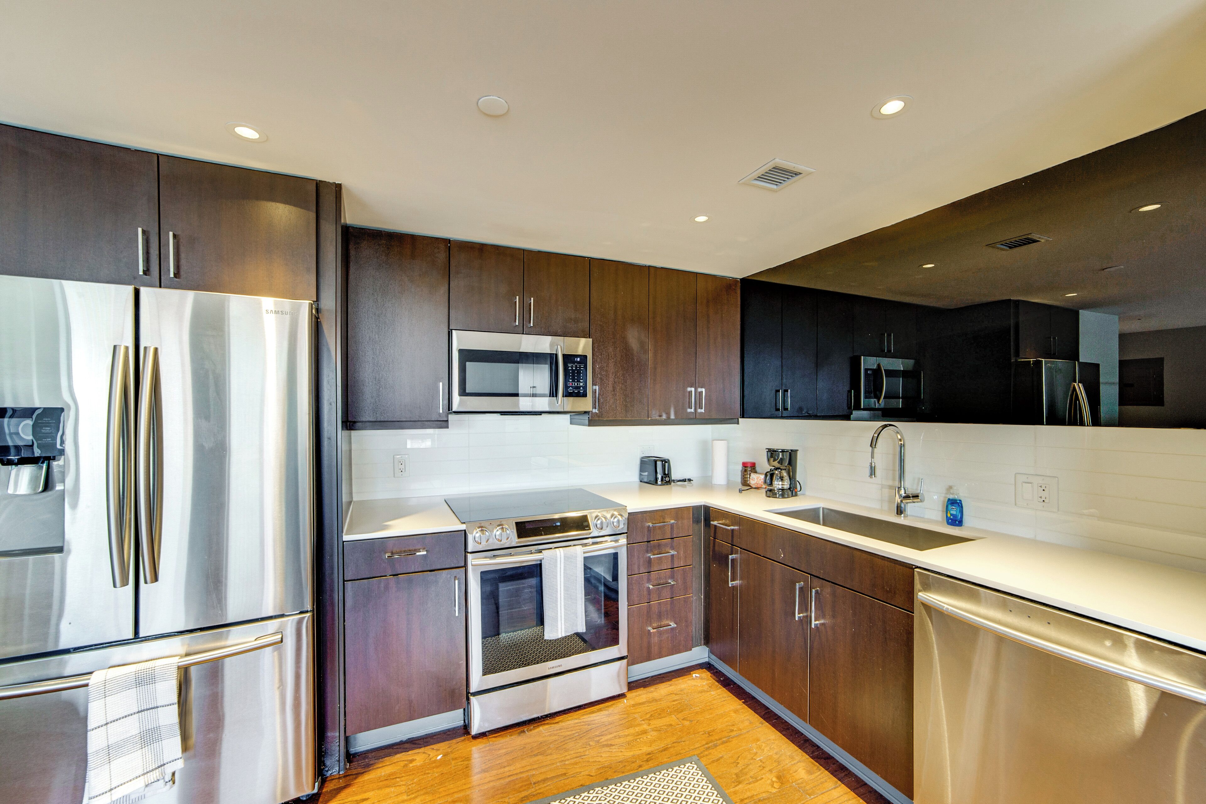 A modern kitchen with stainless steel appliances, wooden cabinets, and a white countertop.