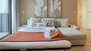 Hotellihuone, jossa on sänky, sohva, ikkuna verhoilla ja kaksi seinätaideteosta.