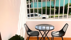 Een balkon met een tafel en stoelen, een bloempot en uitzicht op een straat met geparkeerde auto's.