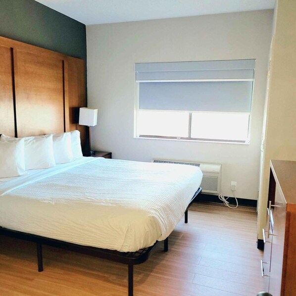 Une chambre d’hôtel comprenant un lit, une table de chevet, une lampe, une fenêtre avec des stores et un radiateur fixé au mur.