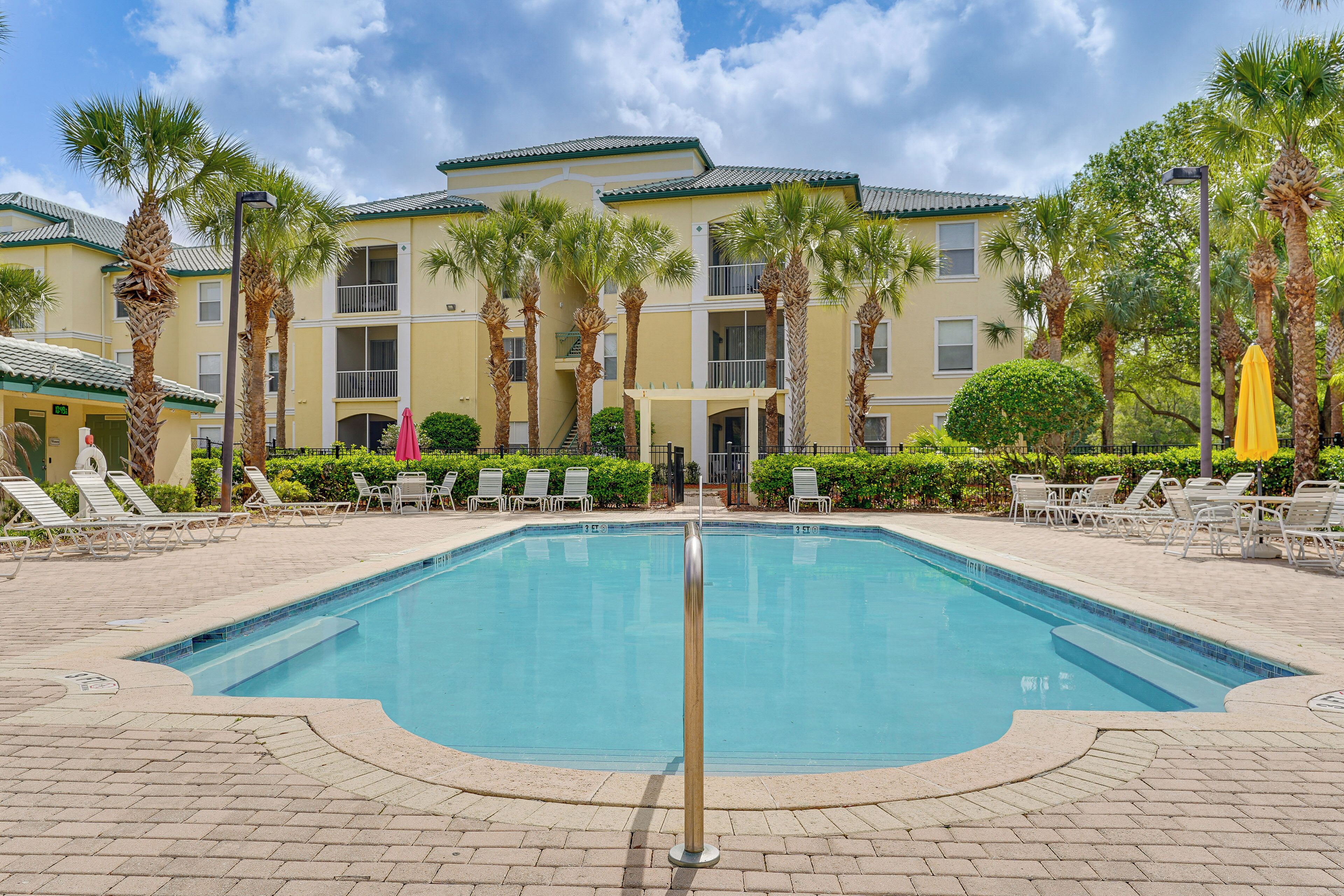 A swimming pool with lounge chairs, palm trees, and a building with balconies.