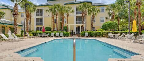 A swimming pool with lounge chairs, palm trees, and a building with balconies.