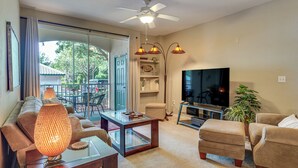 A living room with a sofa, ottoman, coffee table, TV, ceiling fan, and a glass door leading outside. - Pool, Parks & Fun! Family Resort Stay Near Disney (Kissimmee)