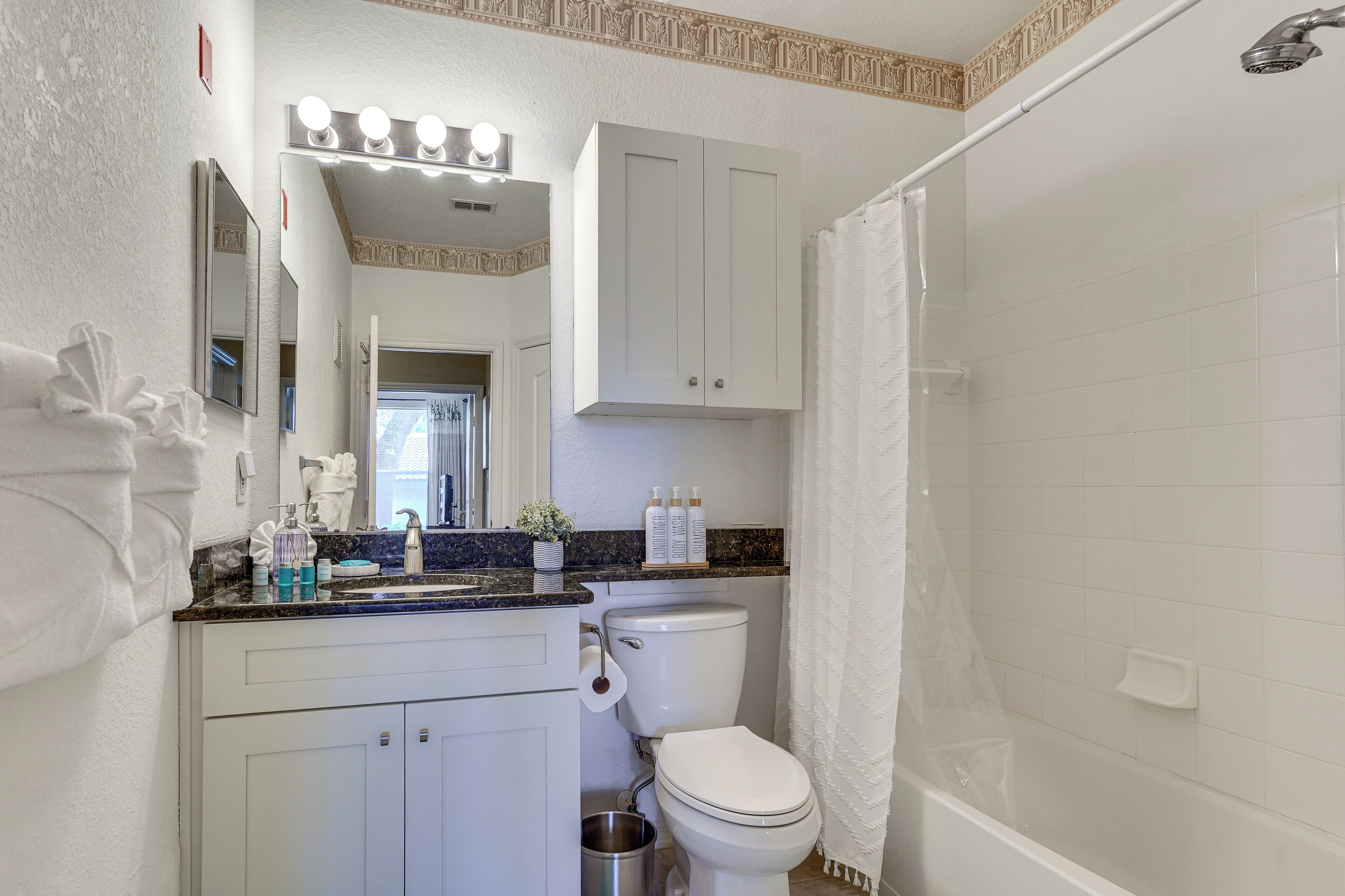 A bathroom with a white toilet, a sink with a mirror above it, a shower curtain, and a vanity with a mirror.