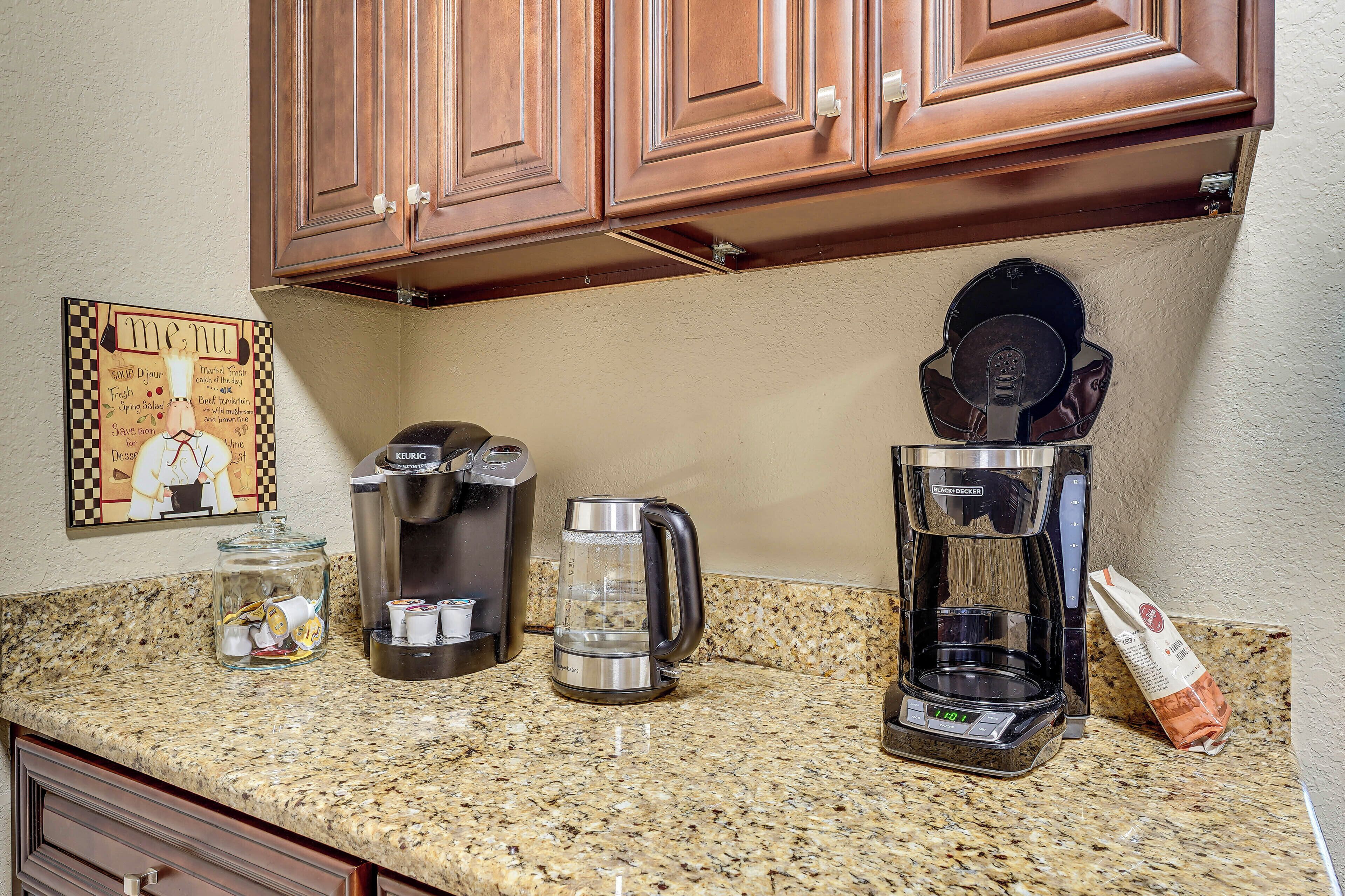 A kitchen with a coffee maker, a kettle, a jar of coffee pods, and a bag of coffee beans.