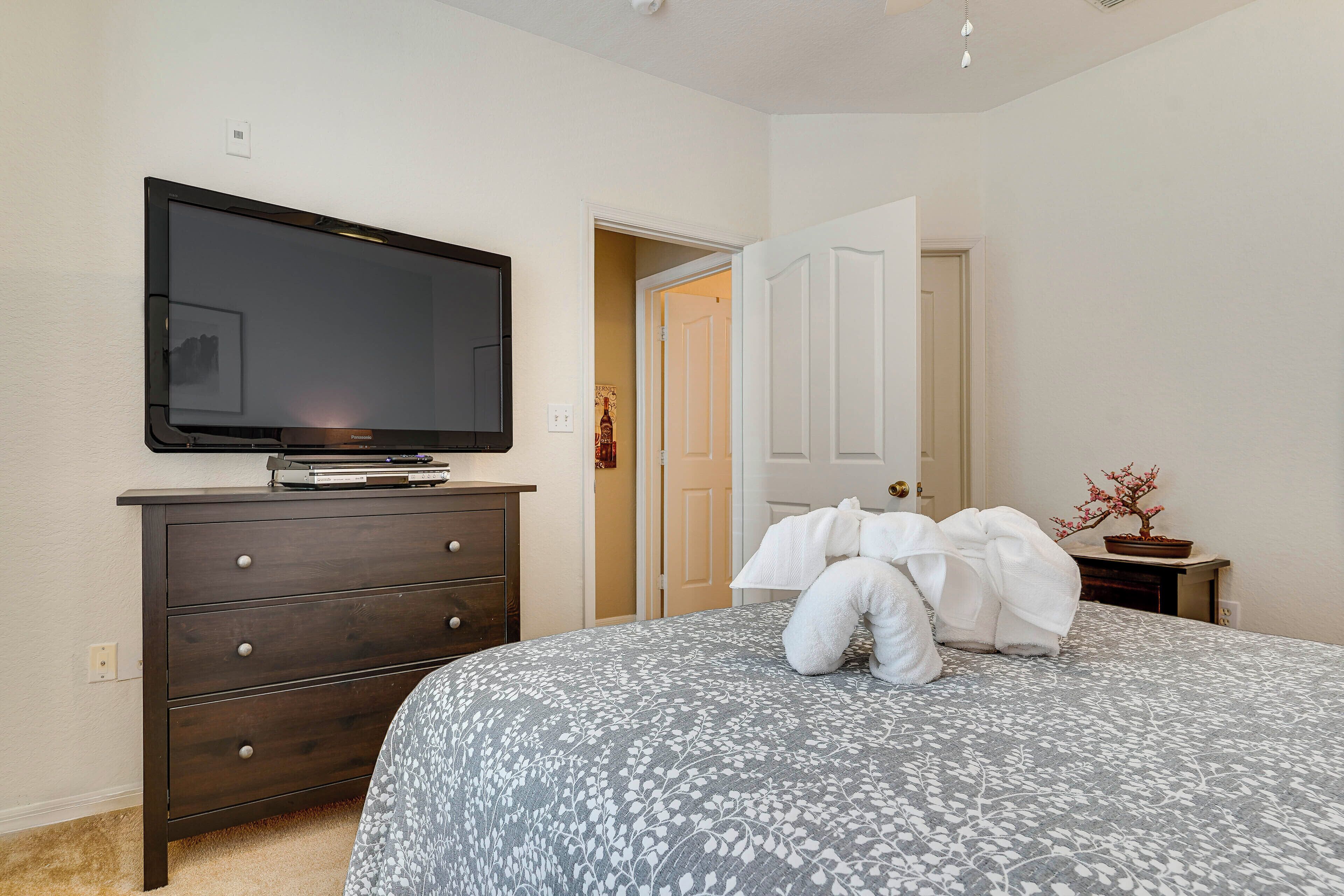 A bedroom with a bed, a dresser, a television, and a door leading to another room.