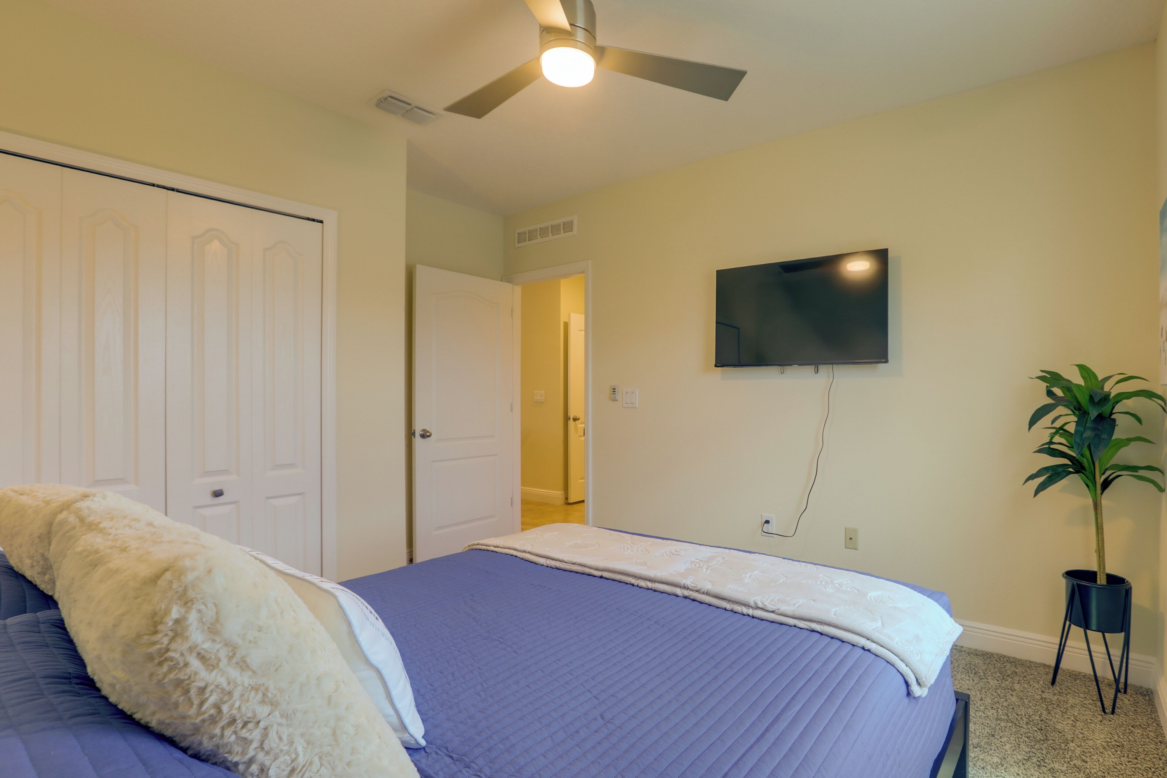 Un dormitorio con una cama, un ventilador de techo, un televisor y una puerta que da a otra habitación.