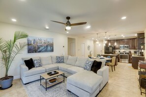 Ein modernes Wohnzimmer mit einem Ecksofa, einem Deckenventilator und einem Essbereich mit Tisch und Stühlen.