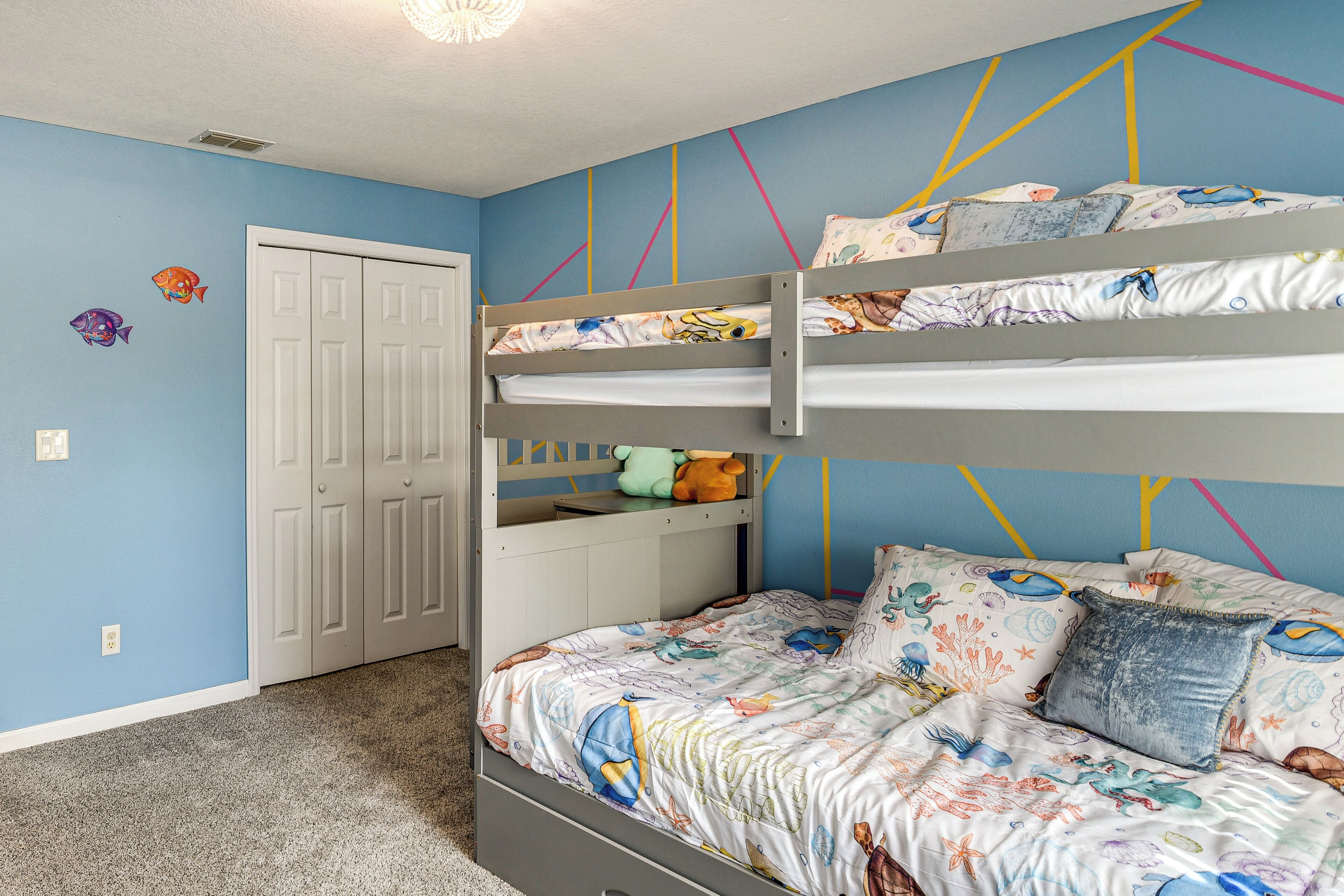 A bunk bed room with a blue wall, a white door, and a bed with a fish-themed bedspread.