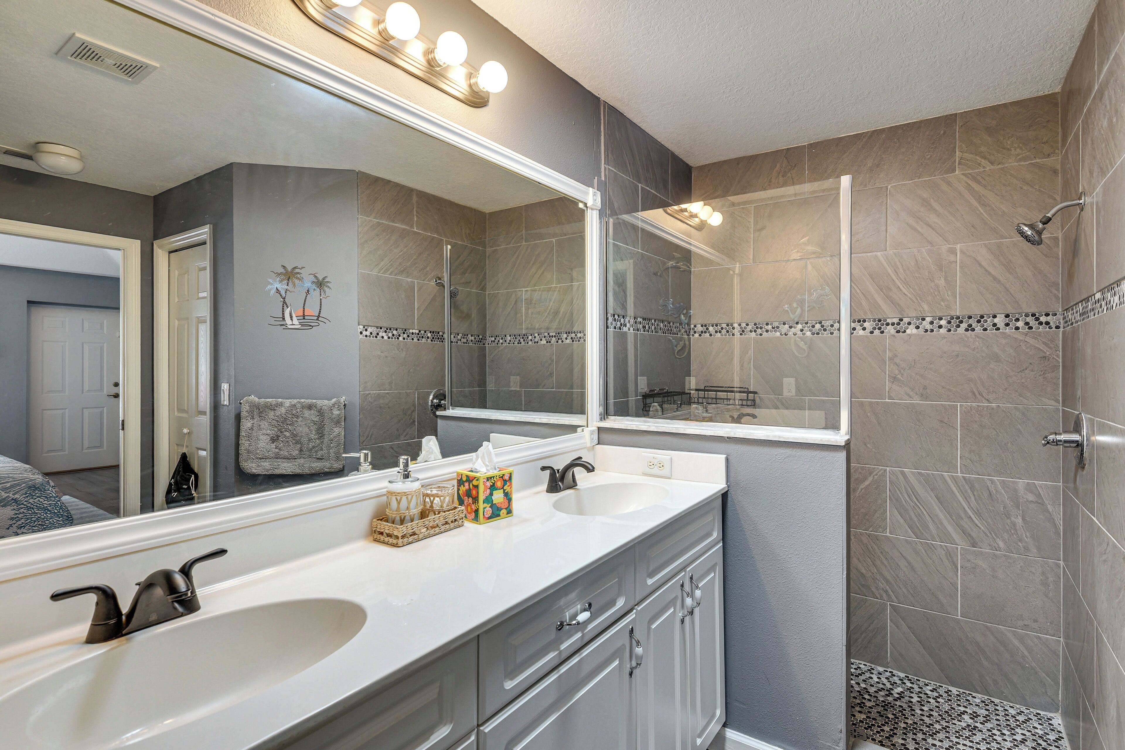 A bathroom with a double sink, a large mirror, and a shower area.