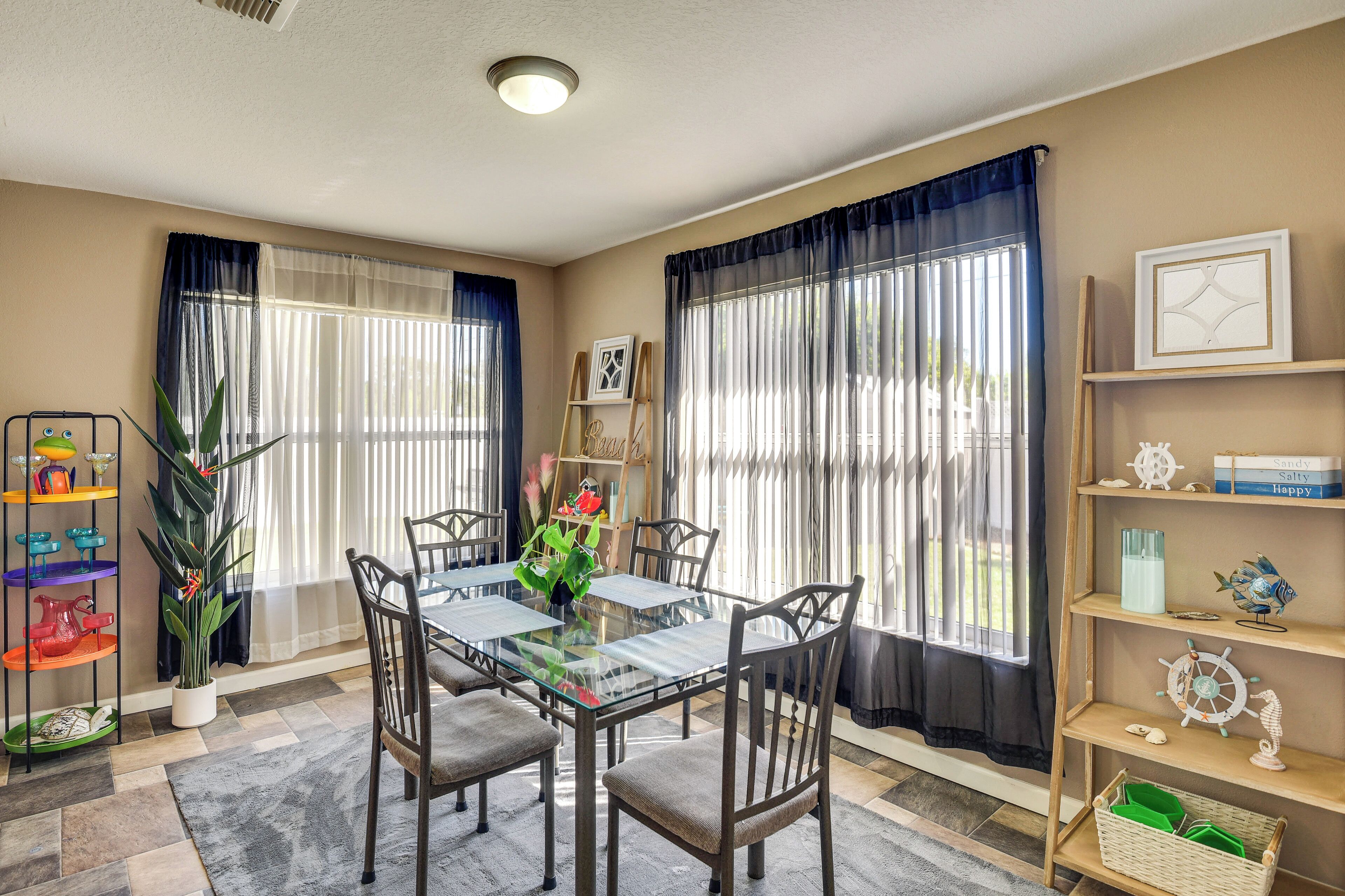 A dining area with a glass table, chairs, a potted plant, and a bookshelf with decorative items.