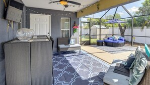A covered patio with a ceiling fan, string lights, a seating area with cushions, and a view of the backyard. - Patio & Poolside Relaxation! Palm Coast Getaway (Palm Coast)