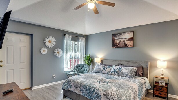 A bedroom with a bed, a nightstand, a chair, a ceiling fan, and a door. - Patio & Poolside Relaxation! Palm Coast Getaway (Palm Coast)
