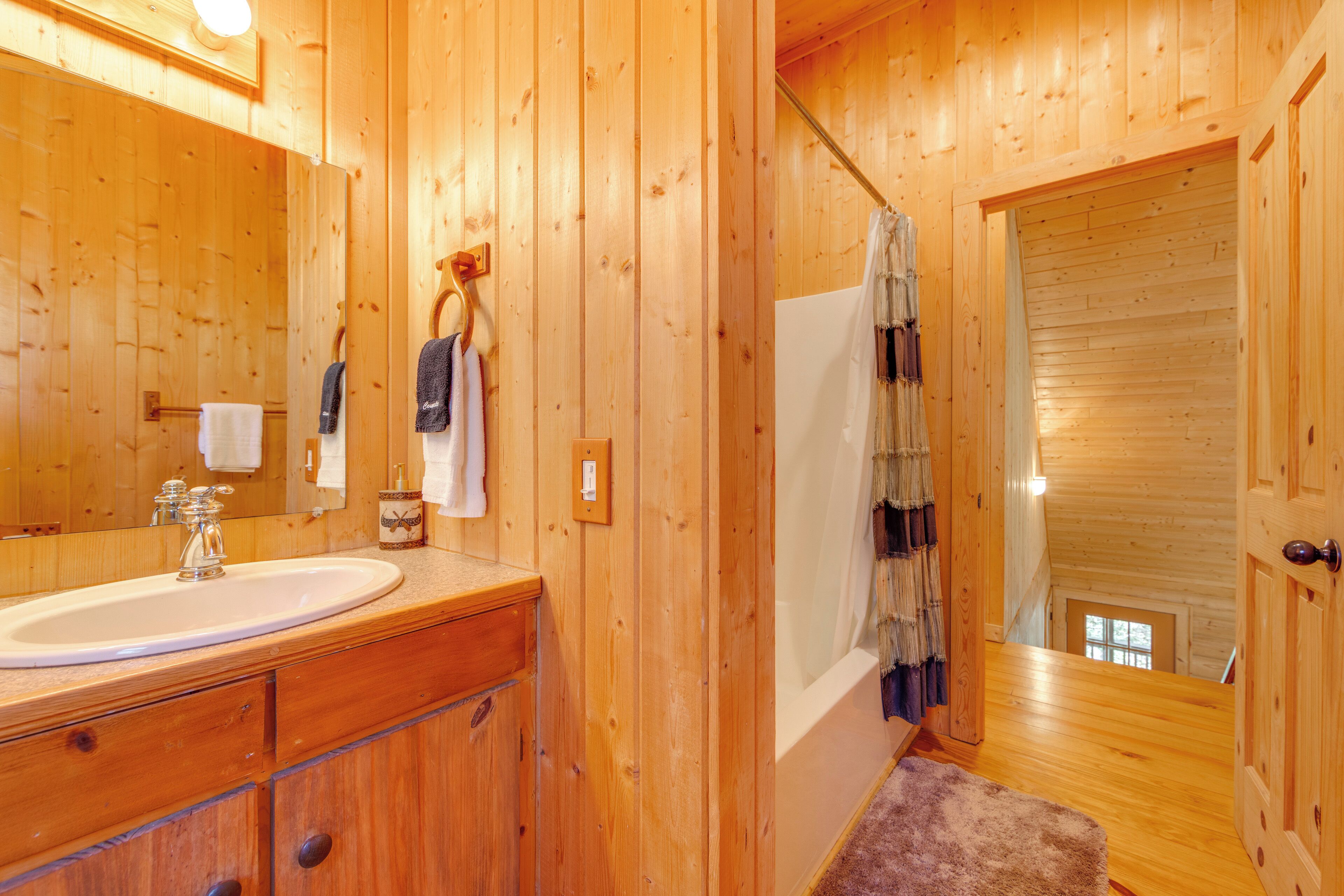 Un baño de cabaña de madera con lavamanos, espejo, toallero y ducha.