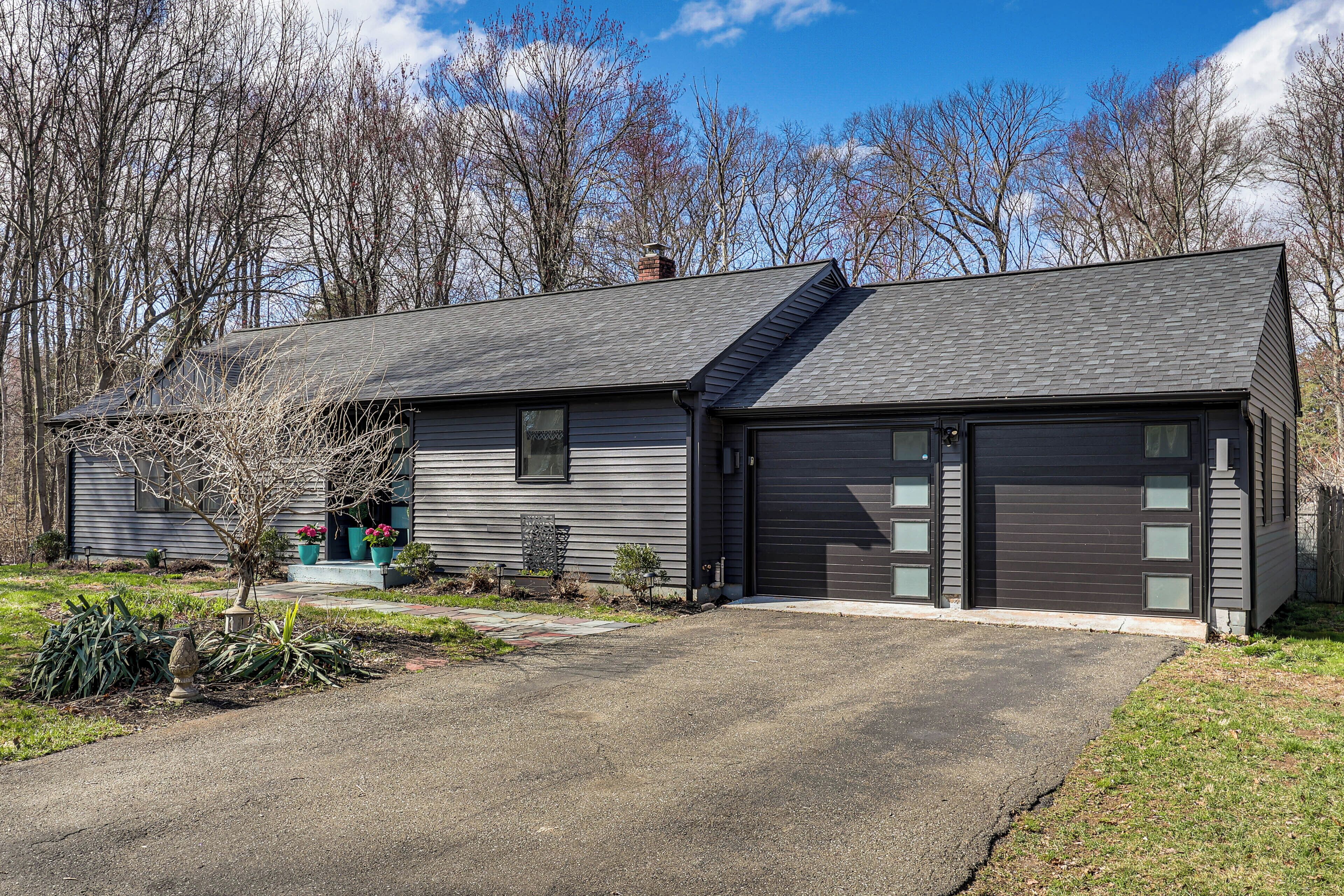A two-story house with a garage, a front yard with a tree and potted plants, and a clear sky.