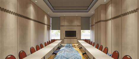 A conference room with a long table, chairs, a TV screen, and patterned carpet.
