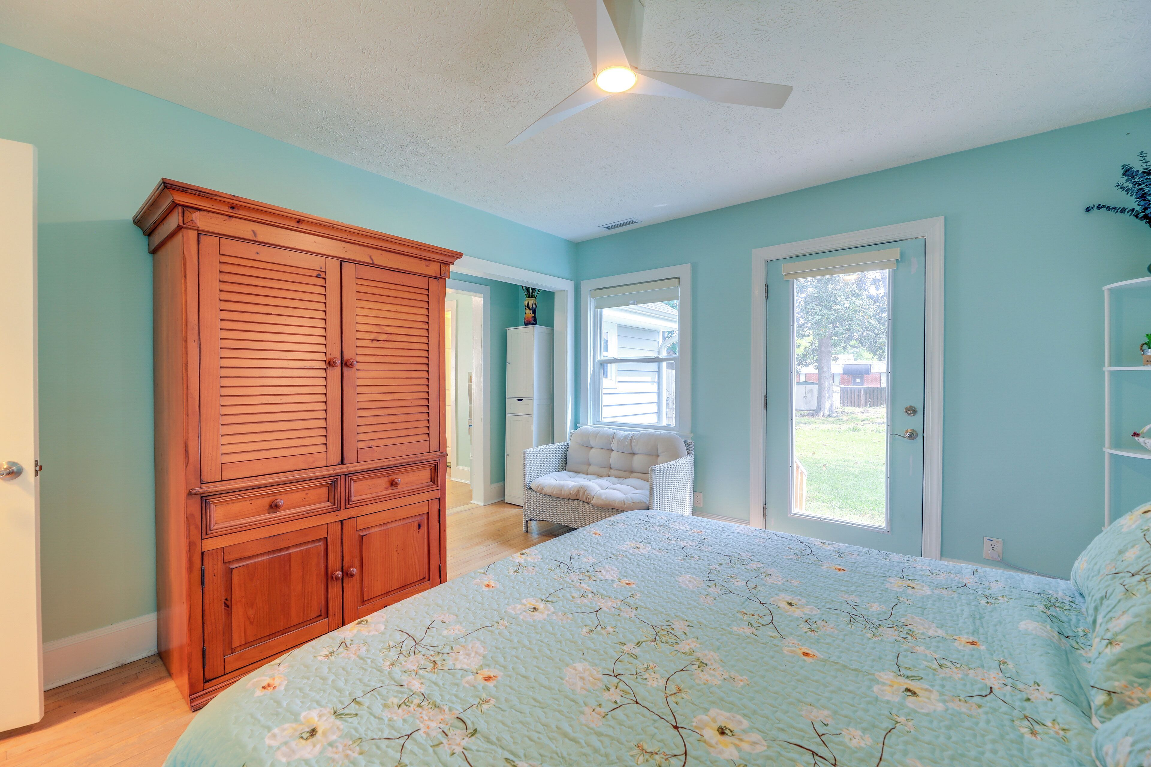 A bedroom with a large bed, a wooden wardrobe, a chair, and a door leading outside.