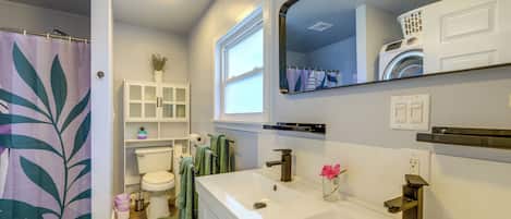 Un baño con lavamanos blanco, espejo y ventana sobre el inodoro.