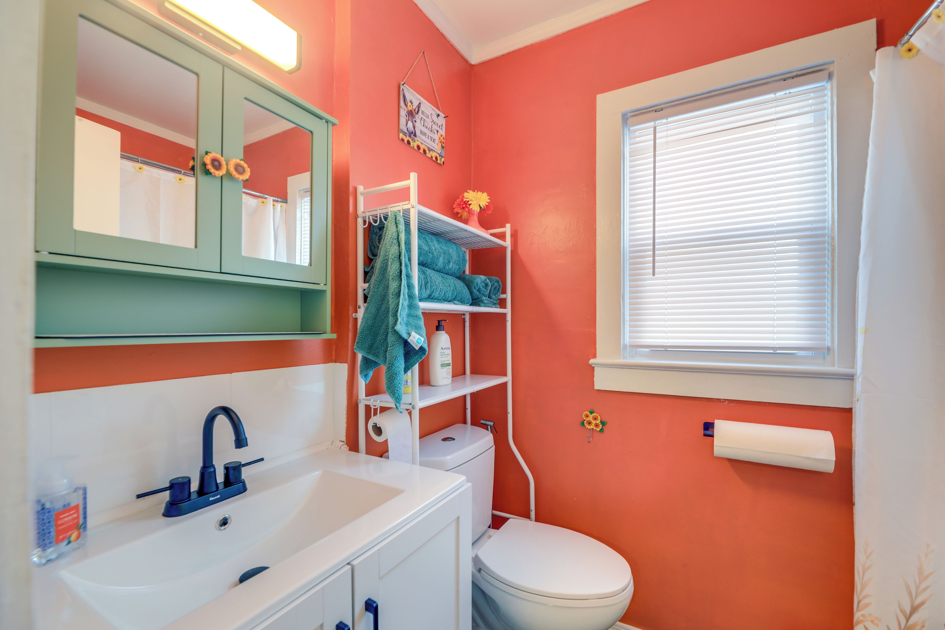 Een badkamer met een wit wastafel, toilet, spiegel en een raam met zonwering.