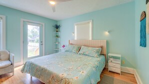 Une chambre à coucher comprenant un lit, une chaise, une table de chevet, une étagère avec des plantes et une porte donnant sur l’extérieur.